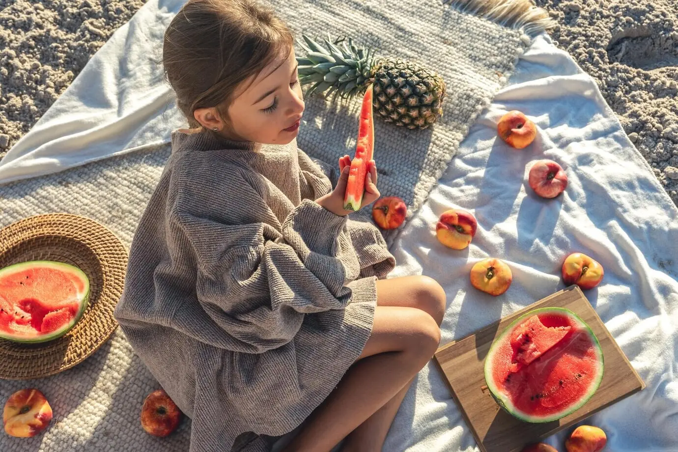 Ein kleines Mädchen isst Obst, während es auf einer Decke am Strand liegt.